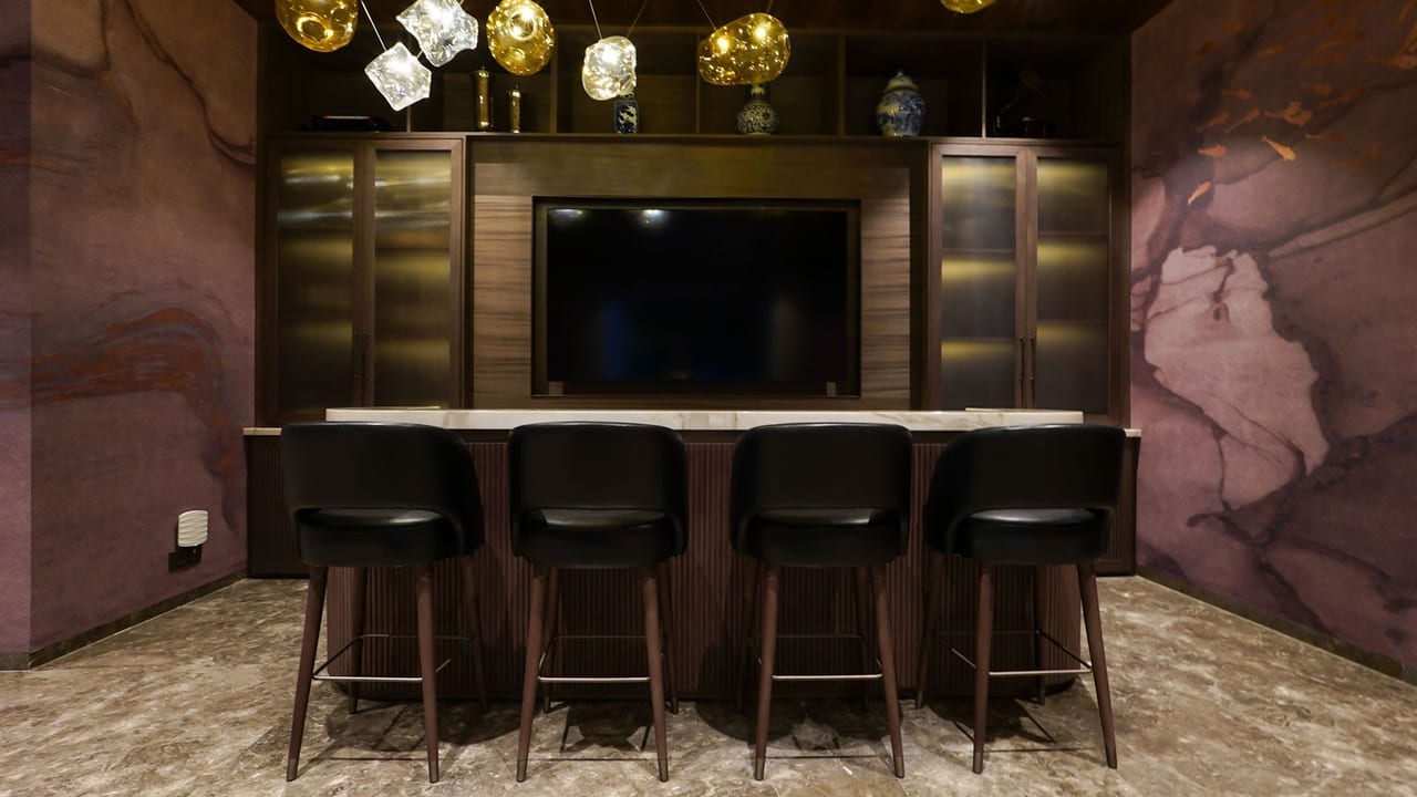 A bar with leather stools beneath a backlit cabinet