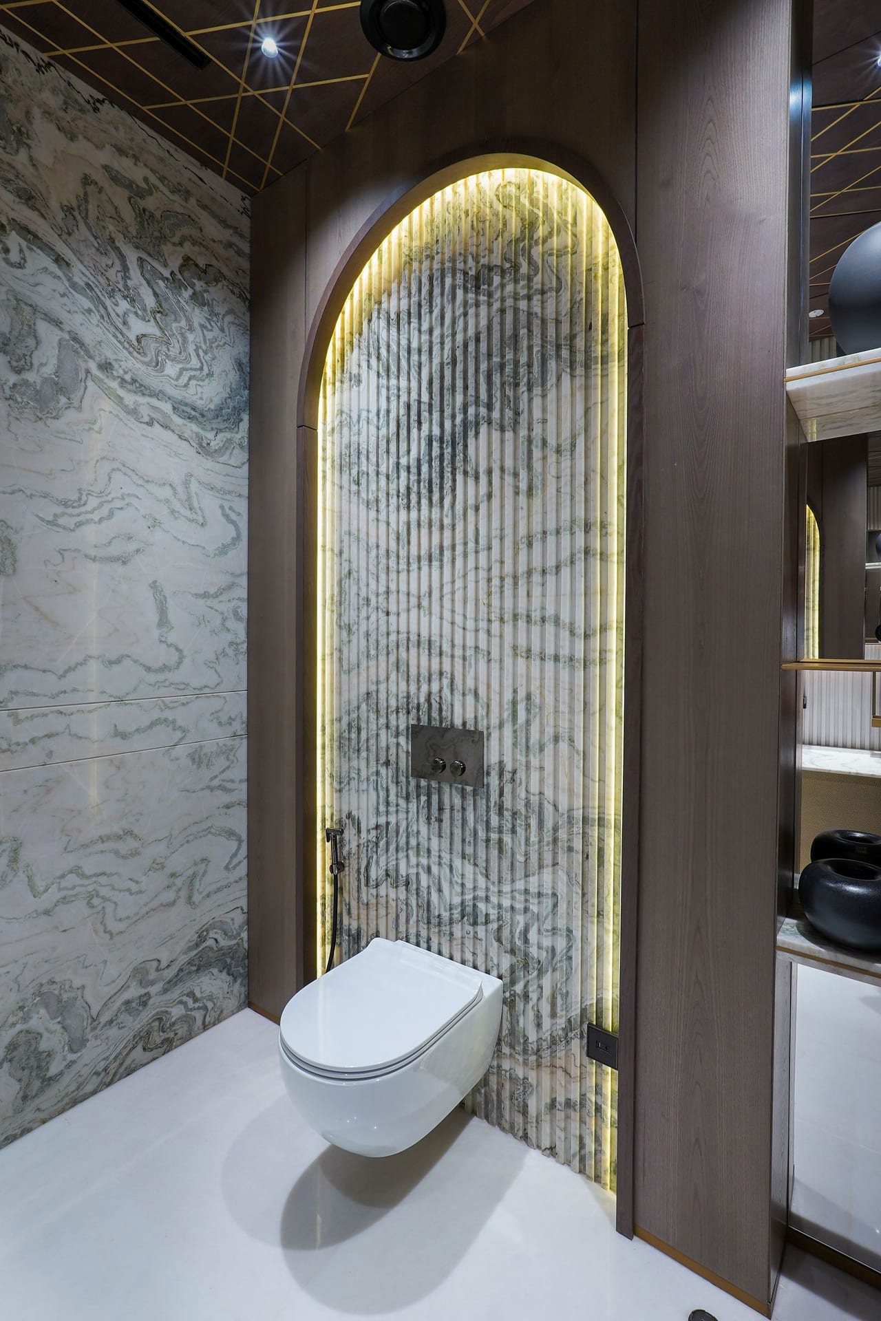 A bathroom with an arched, backlit mirror set into a stone wall