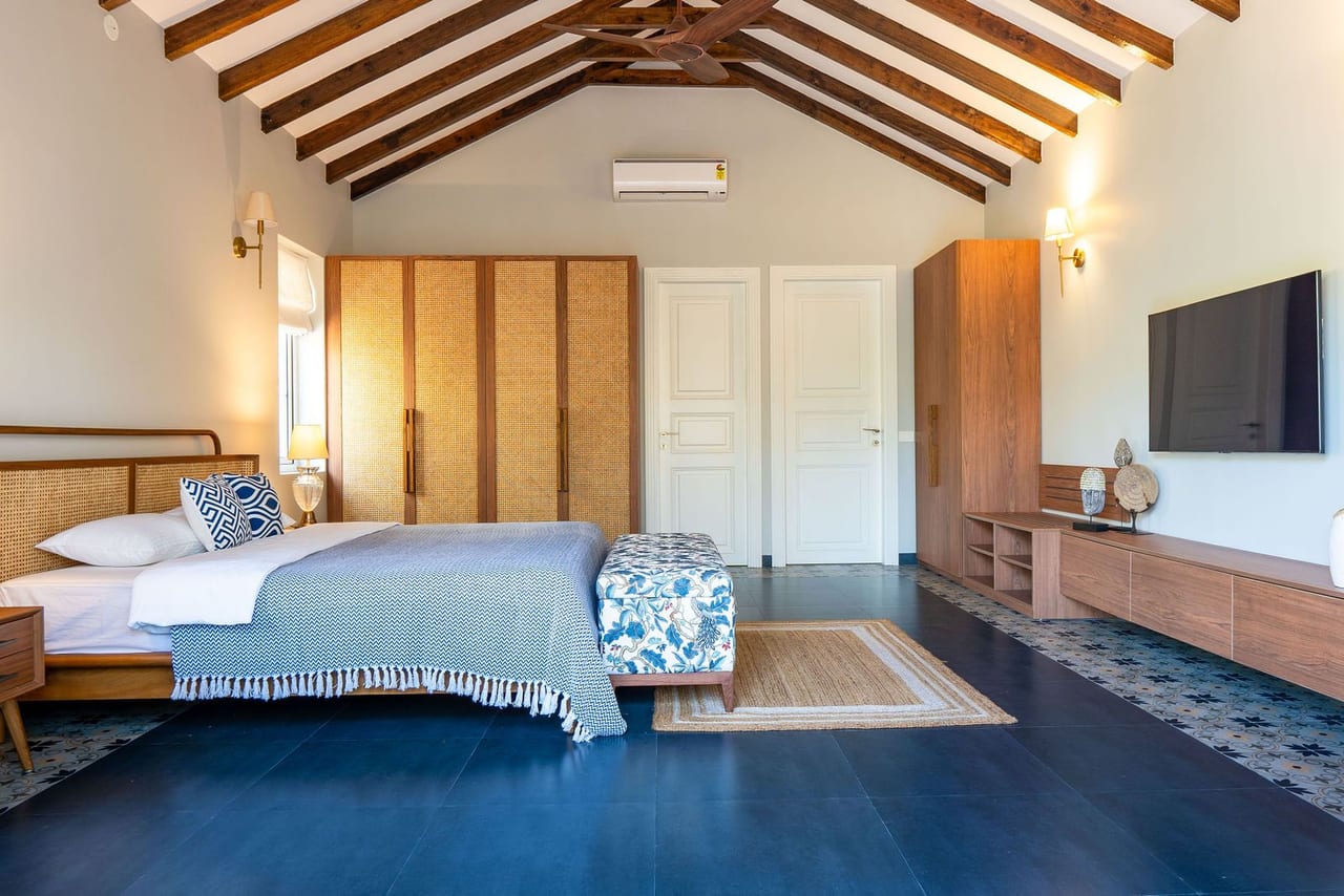 A bedroom under a vaulted timber ceiling, with a blue floor and a patterned bedspread