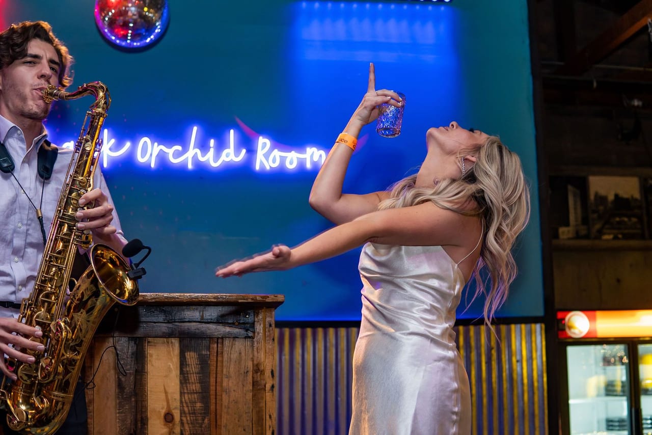 A bride dancing beside a saxophonist under a blue neon sign
