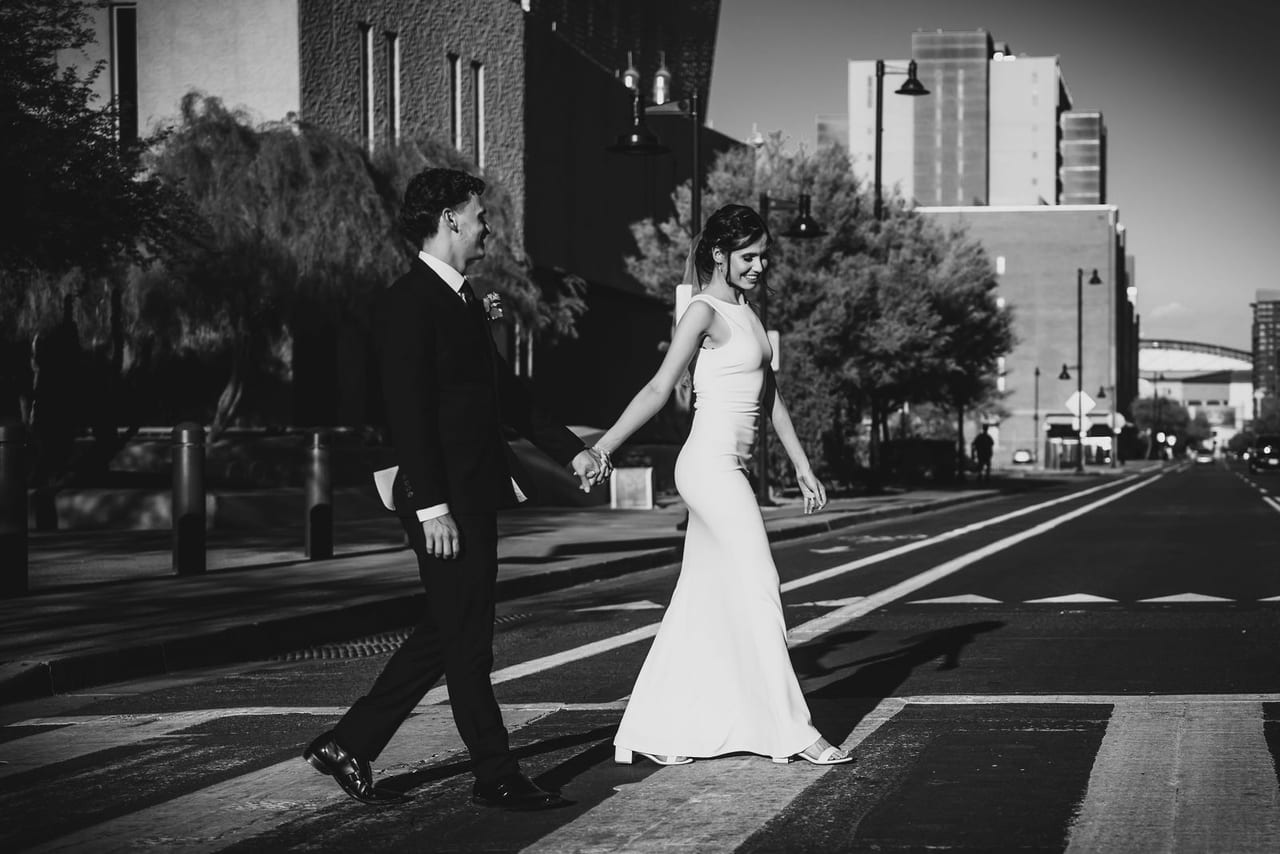 A bride and groom crossing a city street hand in hand, in black and white