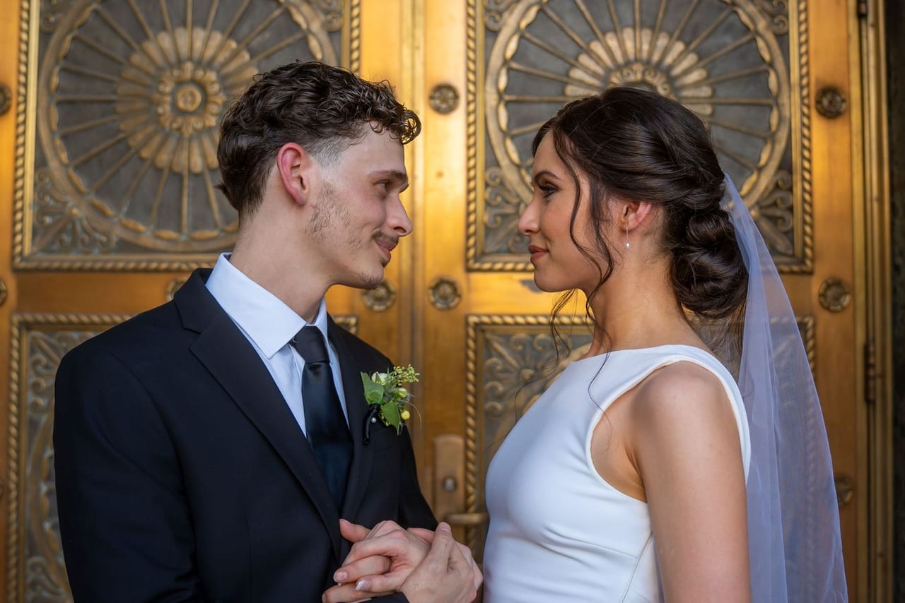 A bride and groom face to face in front of ornate gold doors
