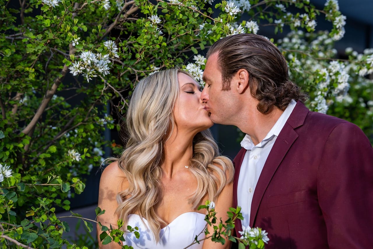 A bride and groom kissing among white flowering shrubs