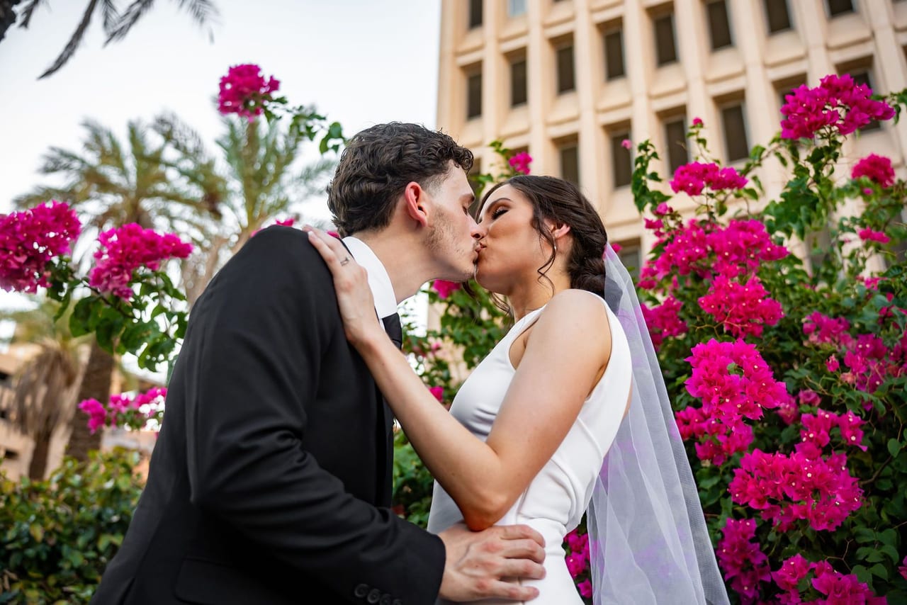 A bride and groom kissing beneath pink bougainvillea