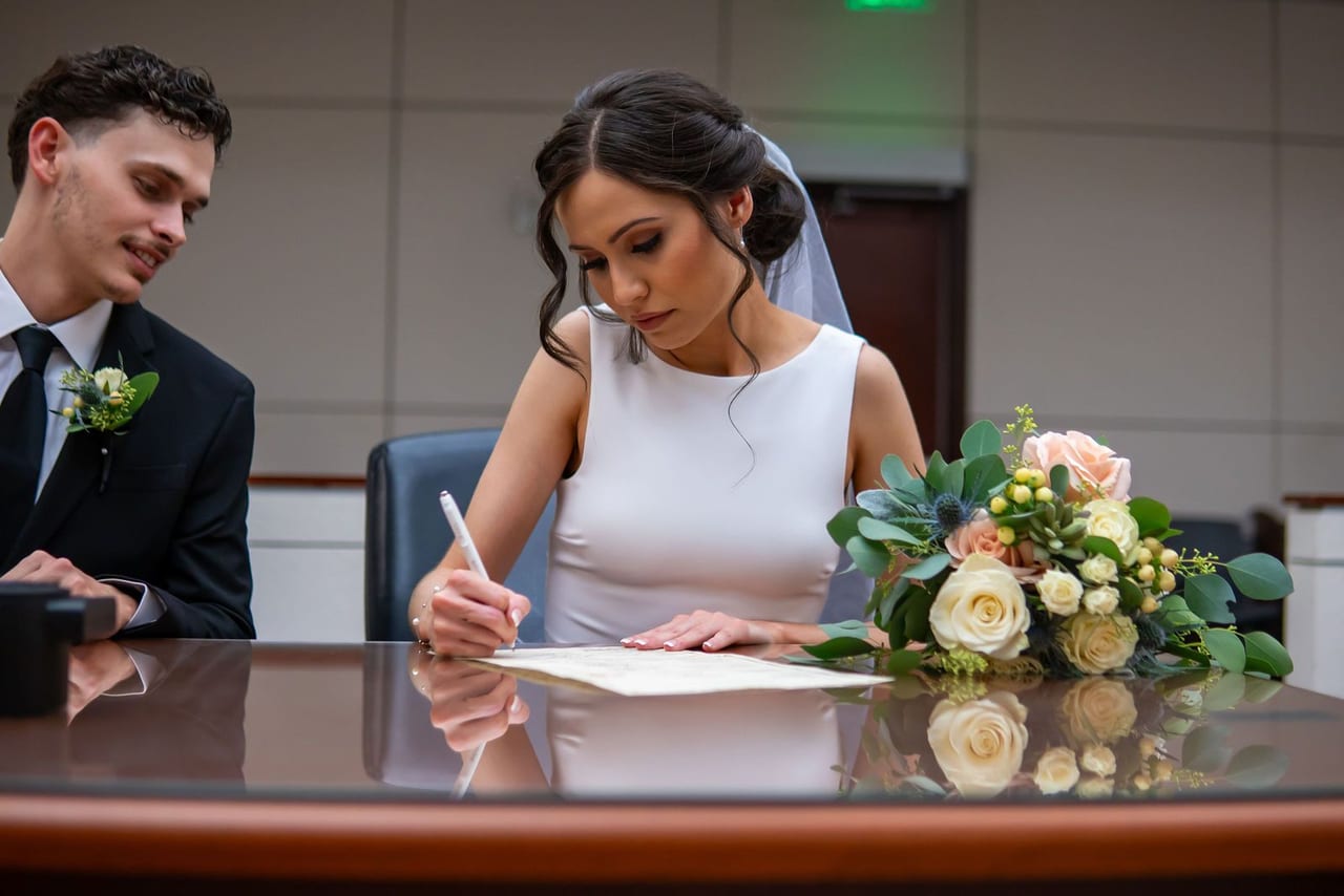 A bride signing the marriage certificate beside her groom