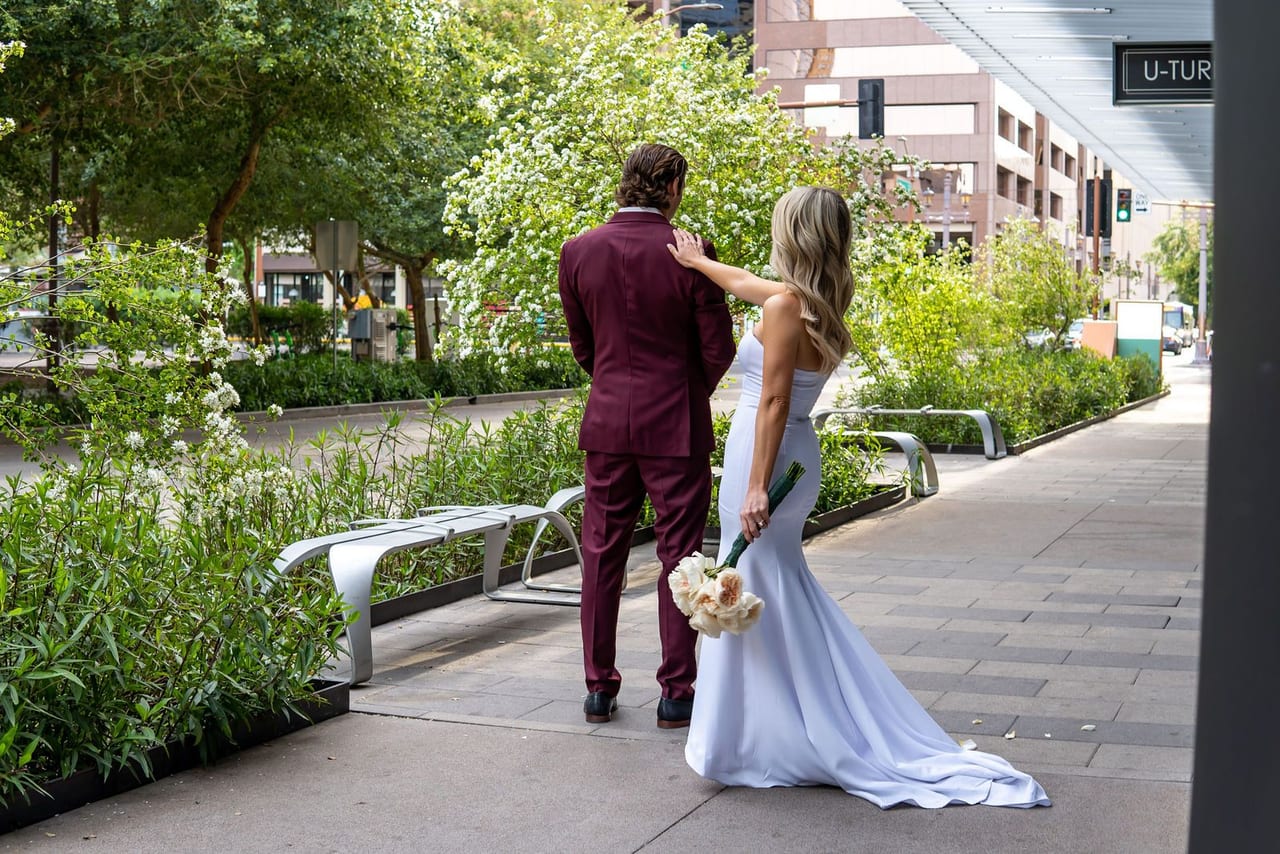A bride walking up behind her groom on a tree-lined city street for the first look
