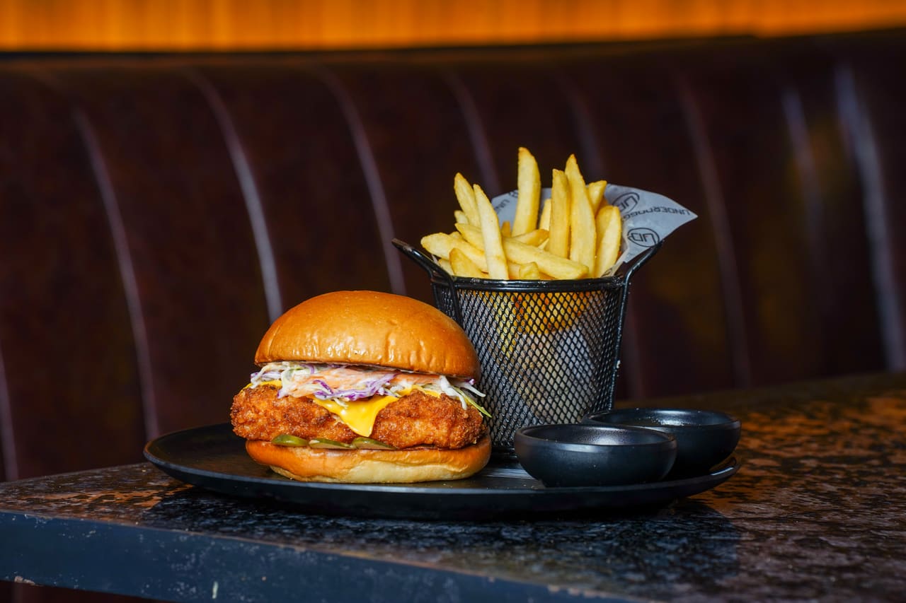 A burger with a cup of fries on a dark marble counter, warm bar lights behind.