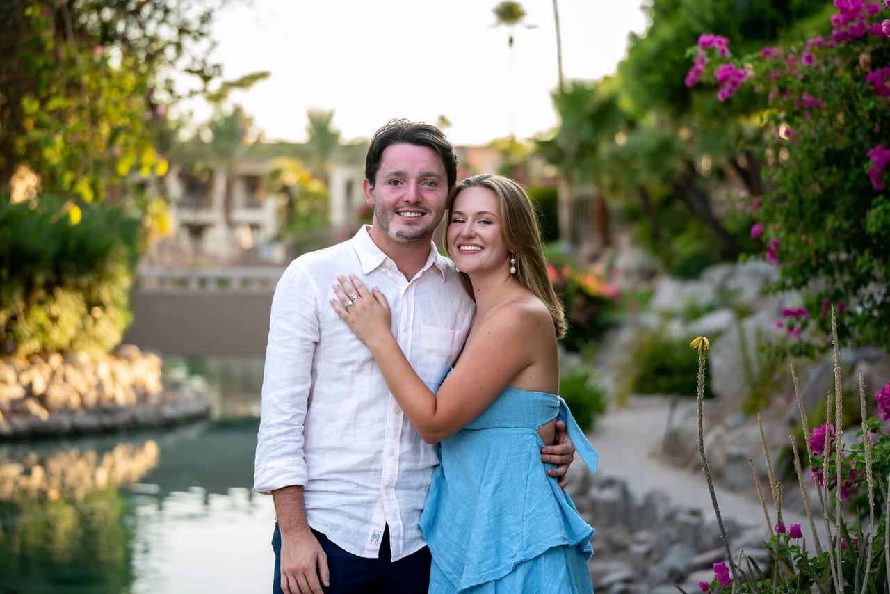A couple embracing beside a garden pond with palms behind them