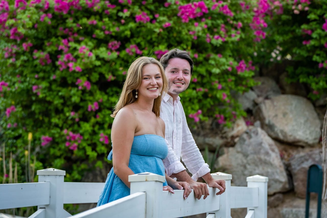A couple leaning on a white bridge beneath pink bougainvillea