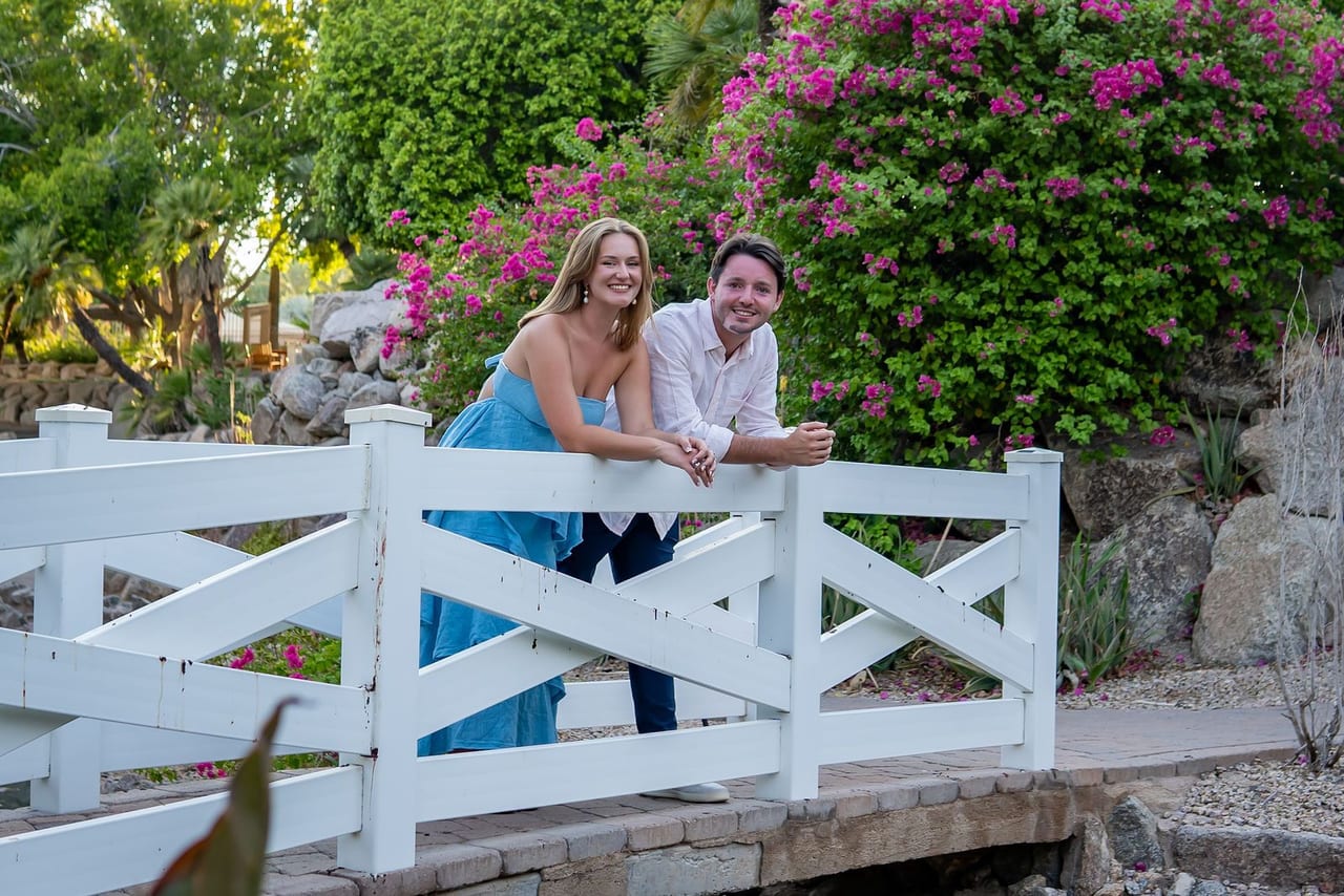 A couple on a white wooden footbridge framed by bougainvillea