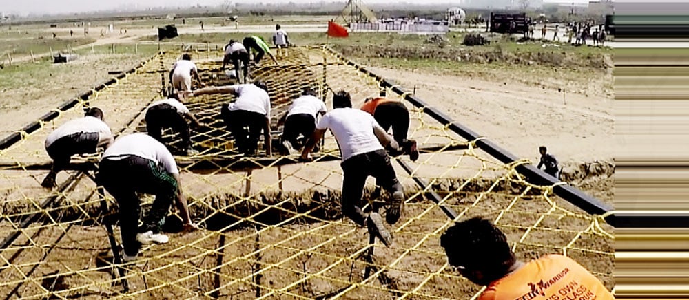 A runner crawling through a cargo net on the Horn Ok Please obstacle