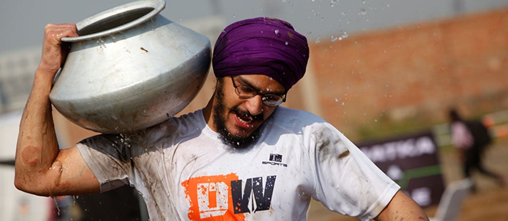 A runner in a purple turban carrying a steel matka on his shoulder on the Matka Mile