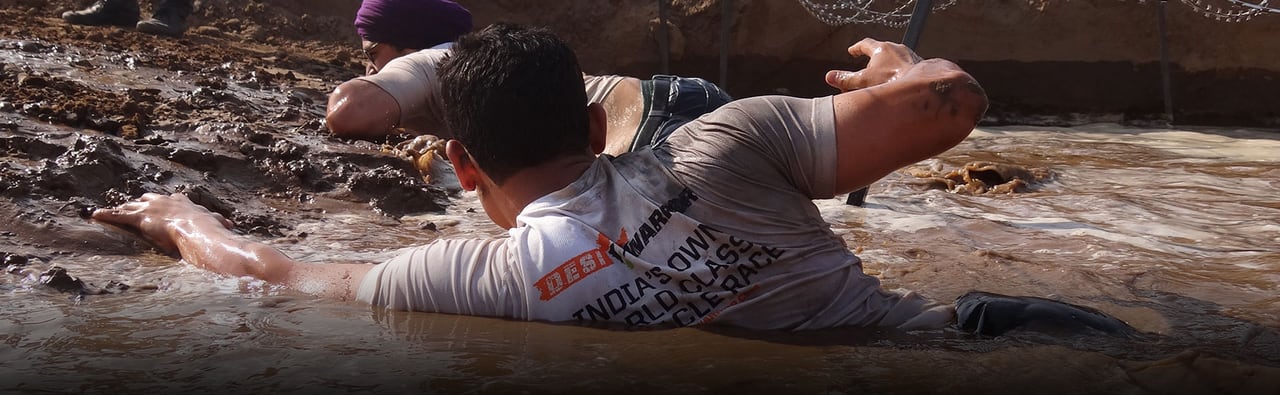 A runner crawling through a muddy pit on the course