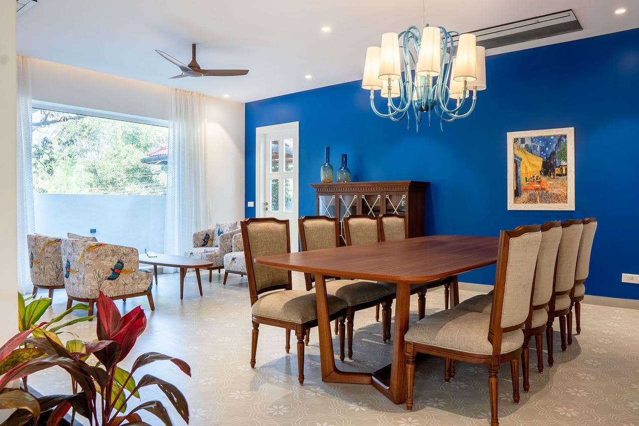 A dining table under a chandelier against a deep blue wall