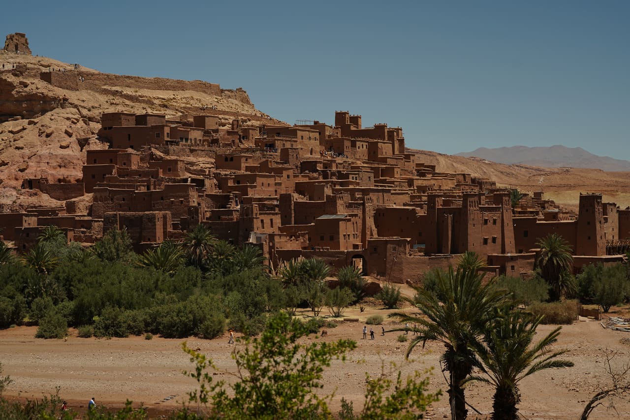 Earthen kasbah buildings stacked on a hillside above a green river valley, Morocco.