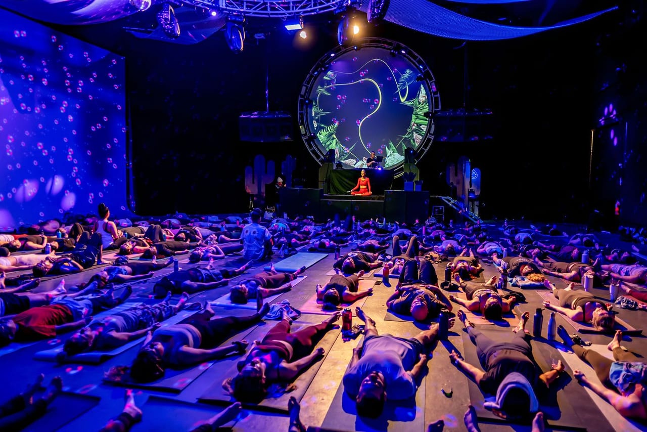 A full room of yoga mats facing a stage with a large projected symbol