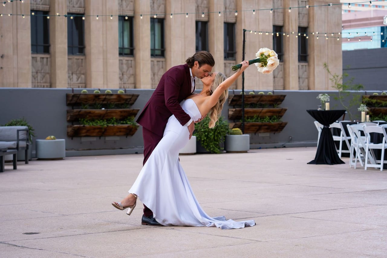 A groom dipping his bride for a kiss on a city rooftop
