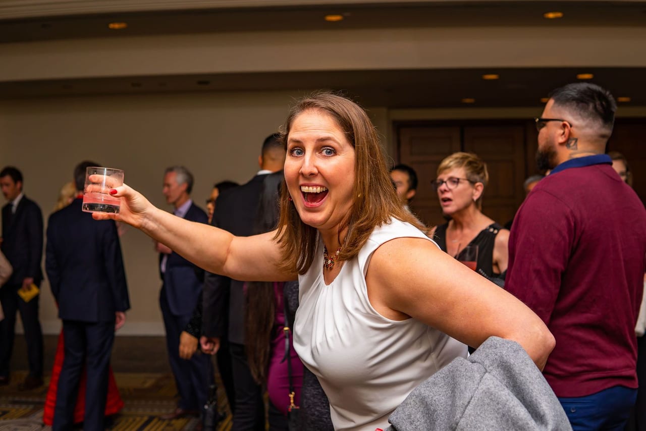 A guest laughing and raising her glass in a hotel ballroom