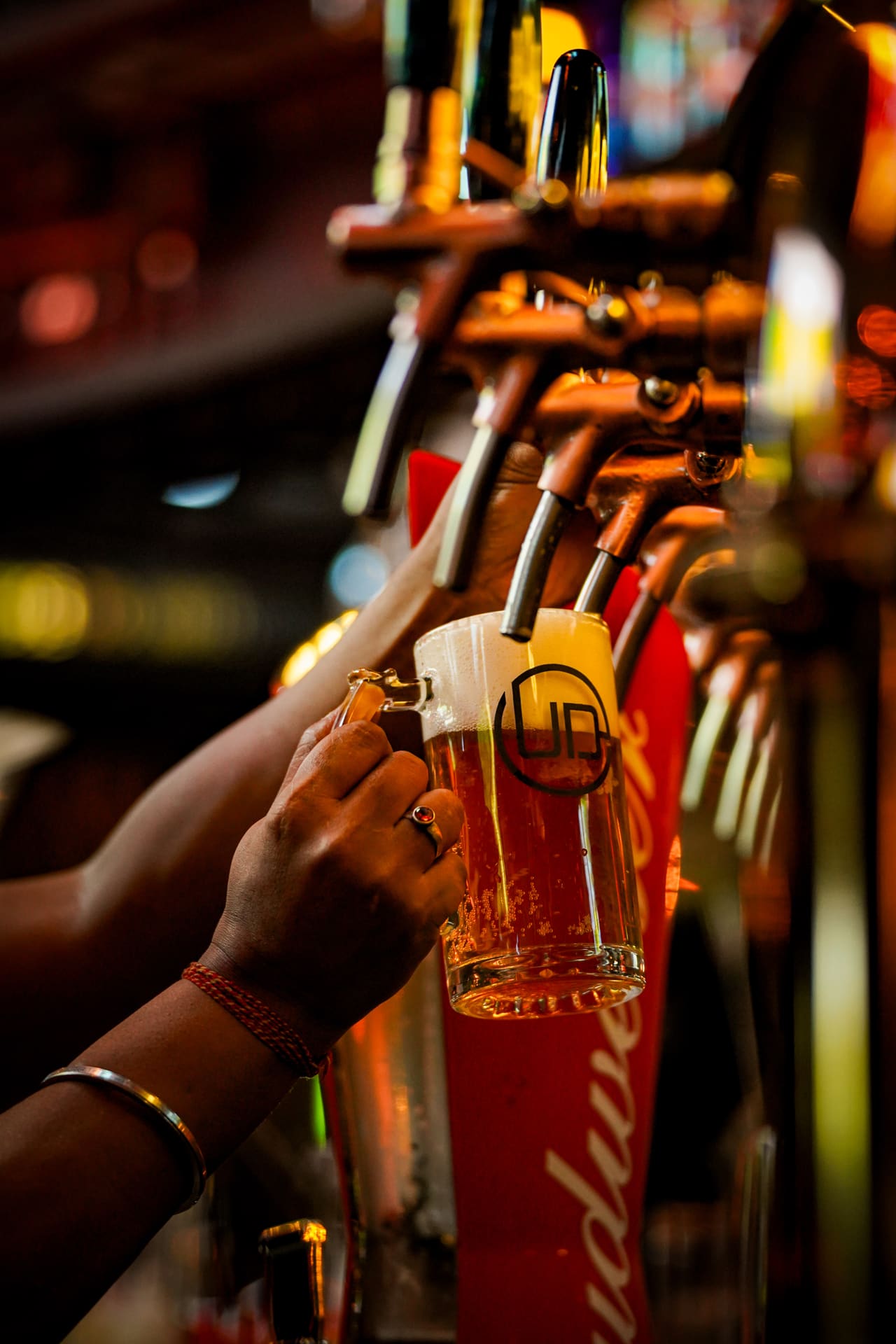 A hand pulling a pint of lager from a row of beer taps under warm light.