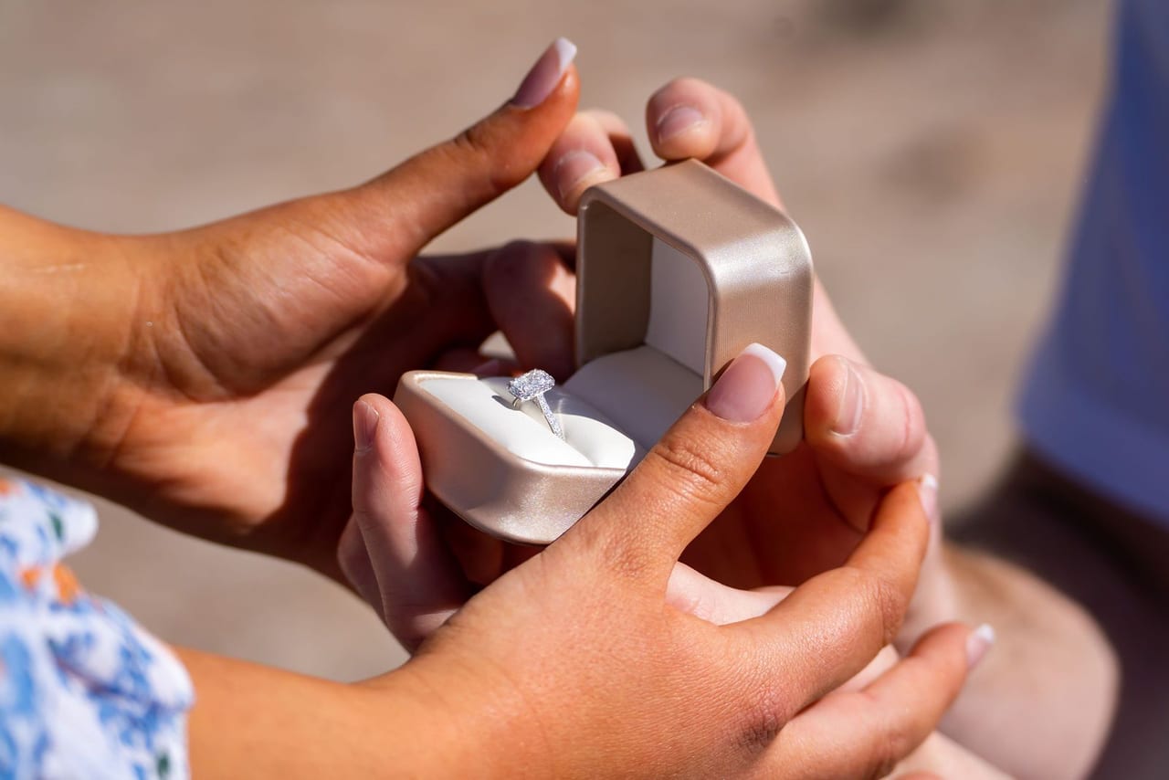 Hands opening a ring box to reveal an engagement ring