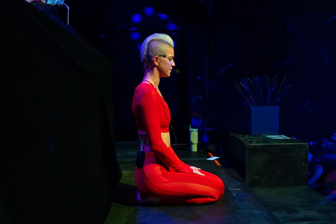 The instructor kneeling on stage in red, lit by a single light