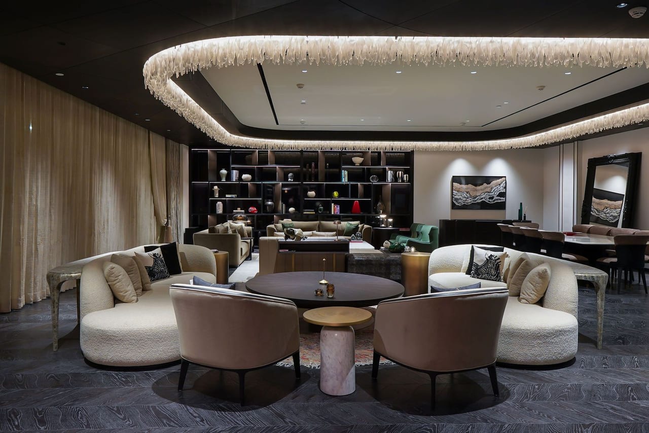 A living room with curved cream sofas beneath a cove-lit ceiling and a wall of shelves