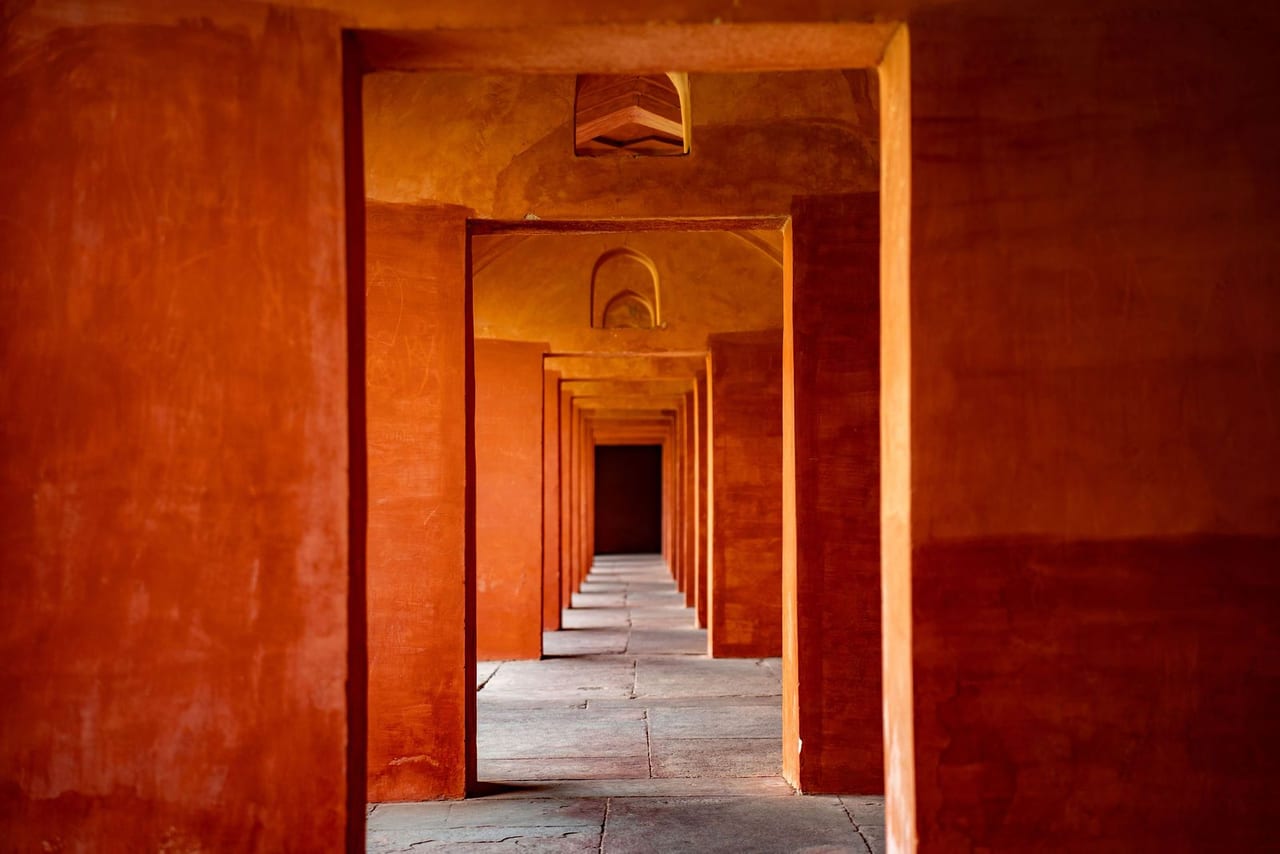 A long corridor of red sandstone arches receding to a doorway