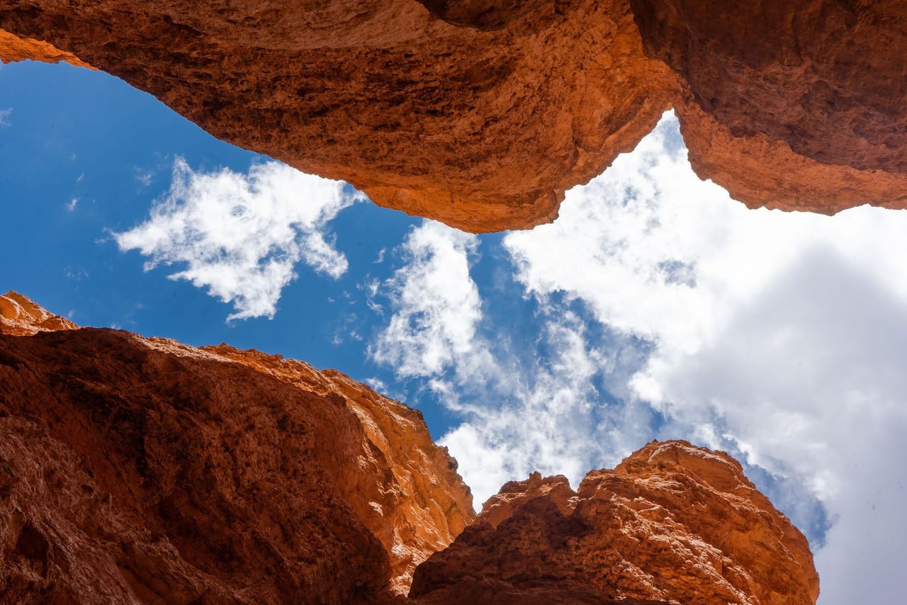 Looking up through a red sandstone arch at white clouds and blue sky