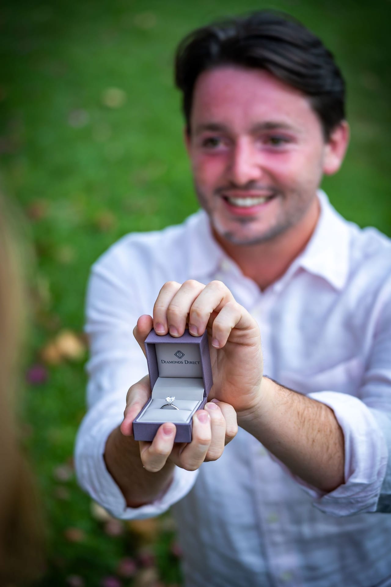 A man holding an open ring box out towards the camera