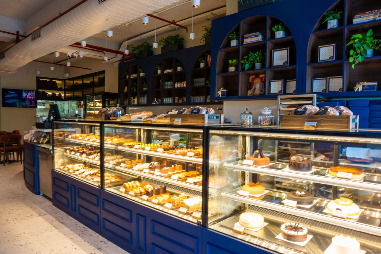 A long glass bakery counter of pastries and cakes set into navy cabinetry, with arched shelving above.