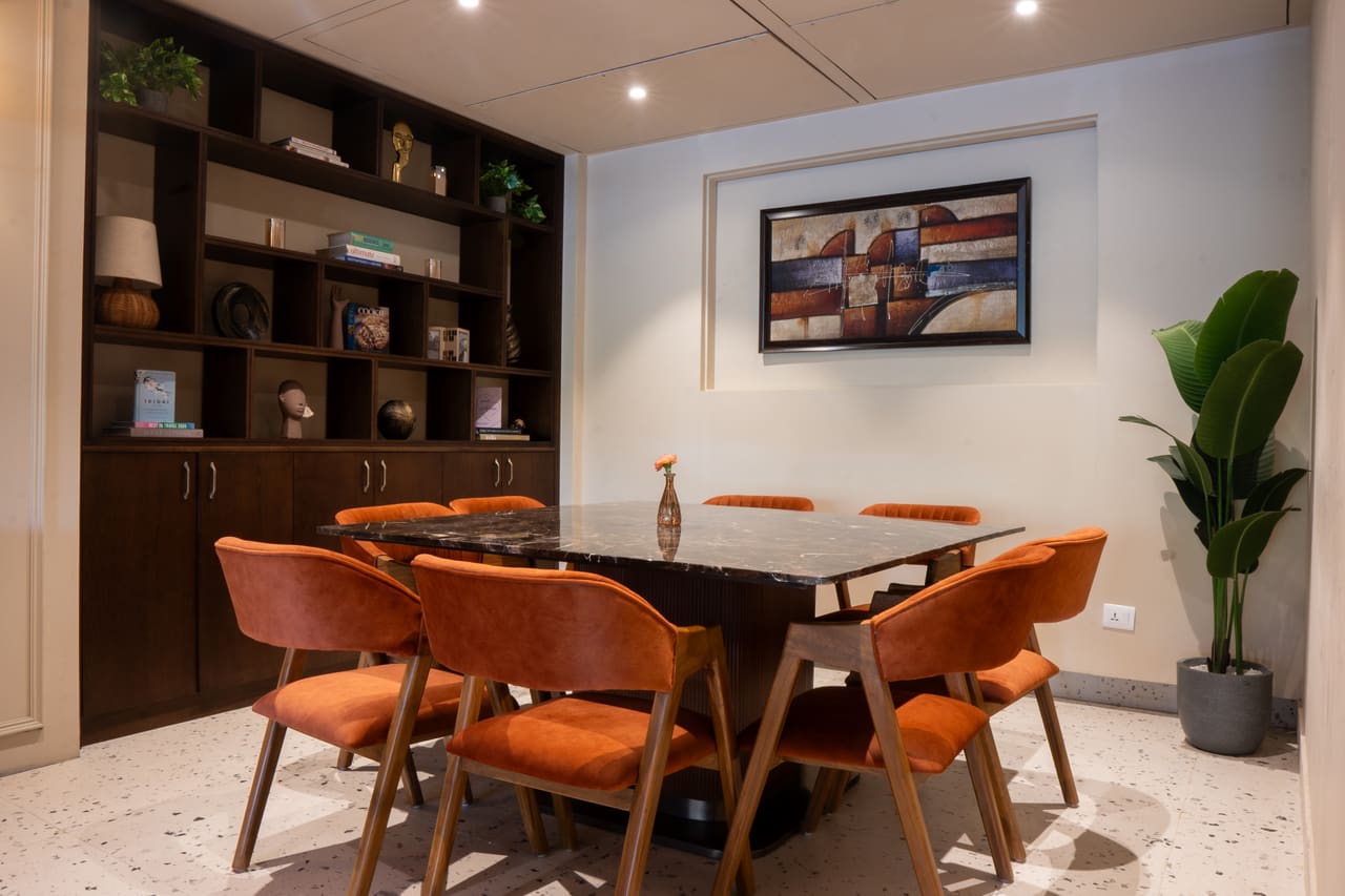 A private dining room with a dark timber table, orange chairs, built-in shelving and a framed artwork.
