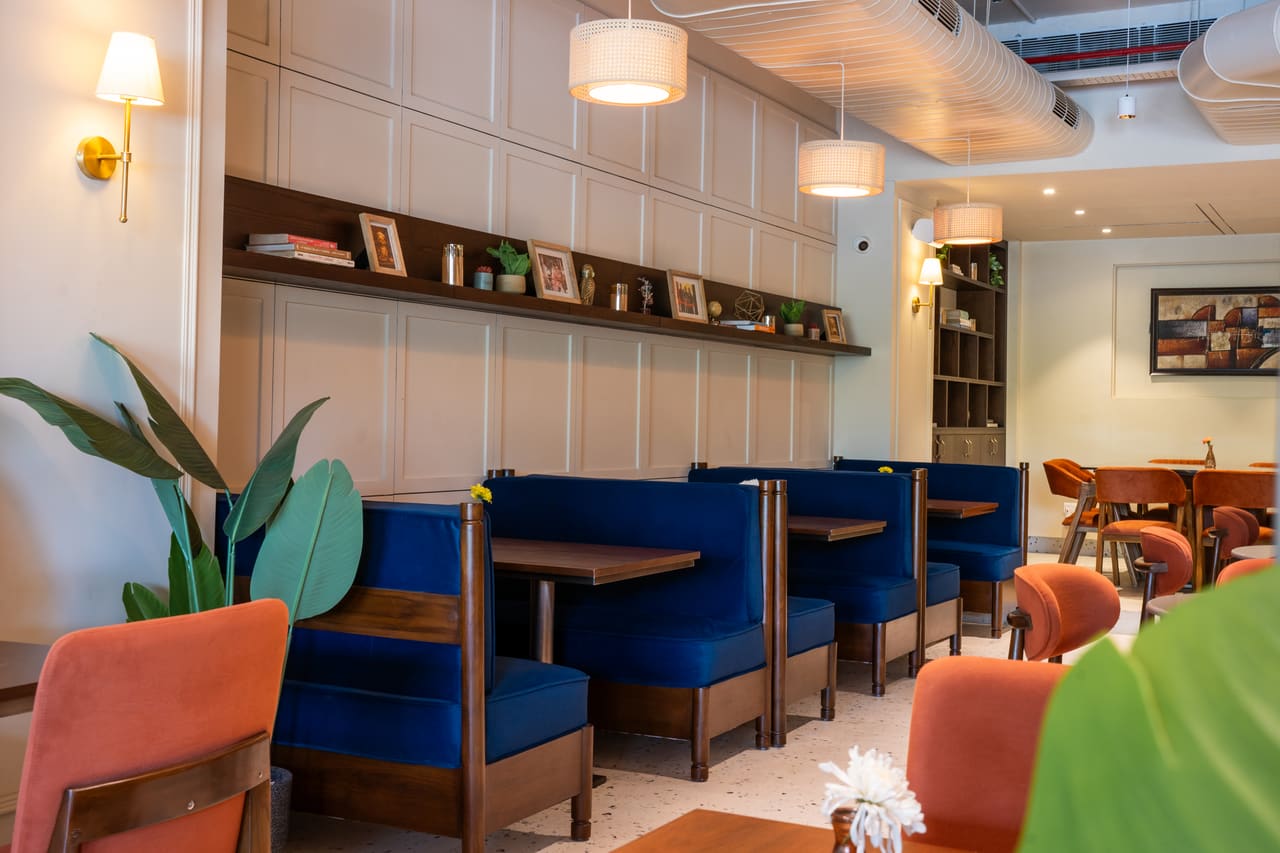 Navy banquette booths along a cream panelled wall with brass sconces and timber tables.
