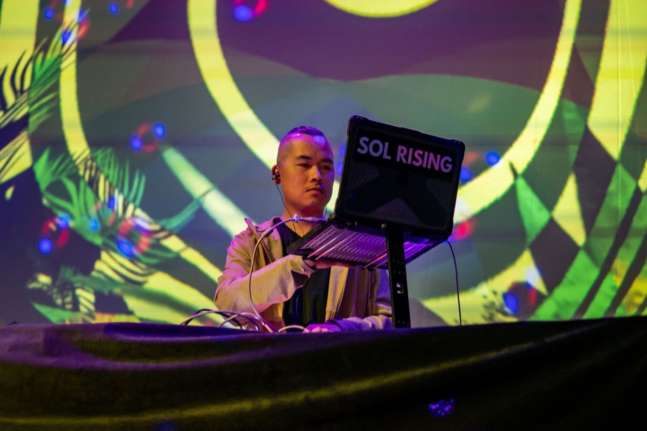 A musician at a keyboard booth lit by green and yellow projections