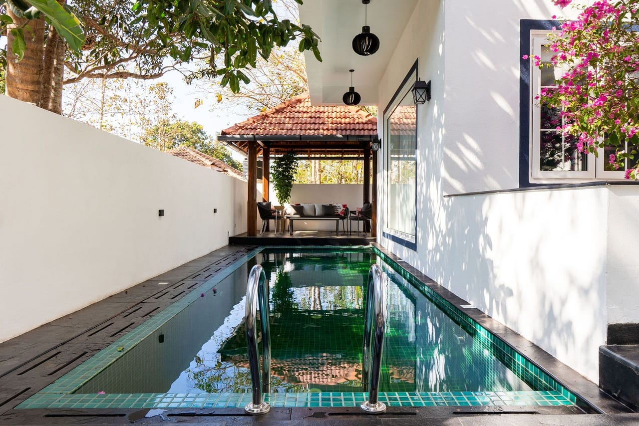 A narrow pool running between white walls to a pavilion with a tiled roof
