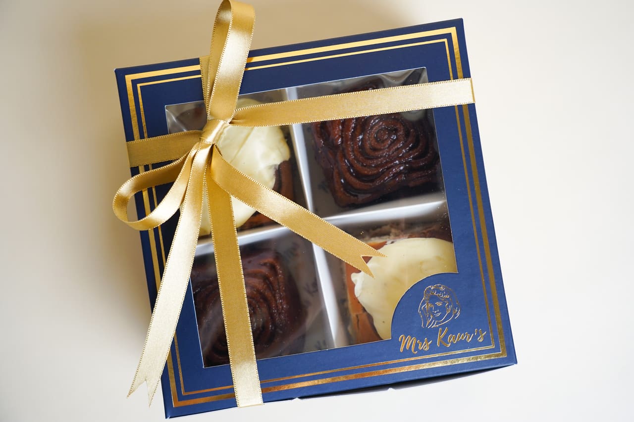 A navy-and-gold Mrs Kaur’s gift box tied with a gold ribbon, on a cream background.