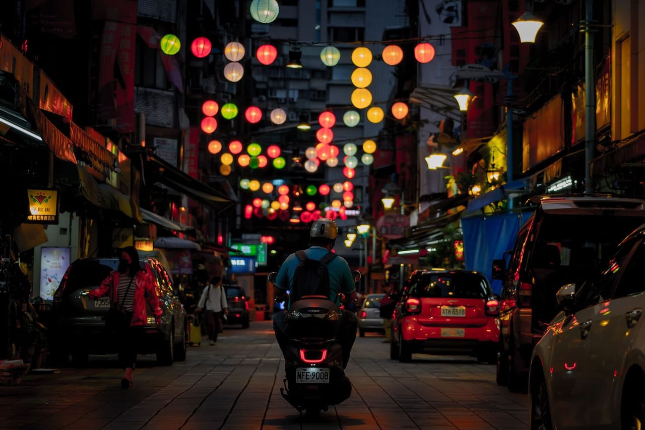 A night street strung with round paper lanterns above scooters and cars