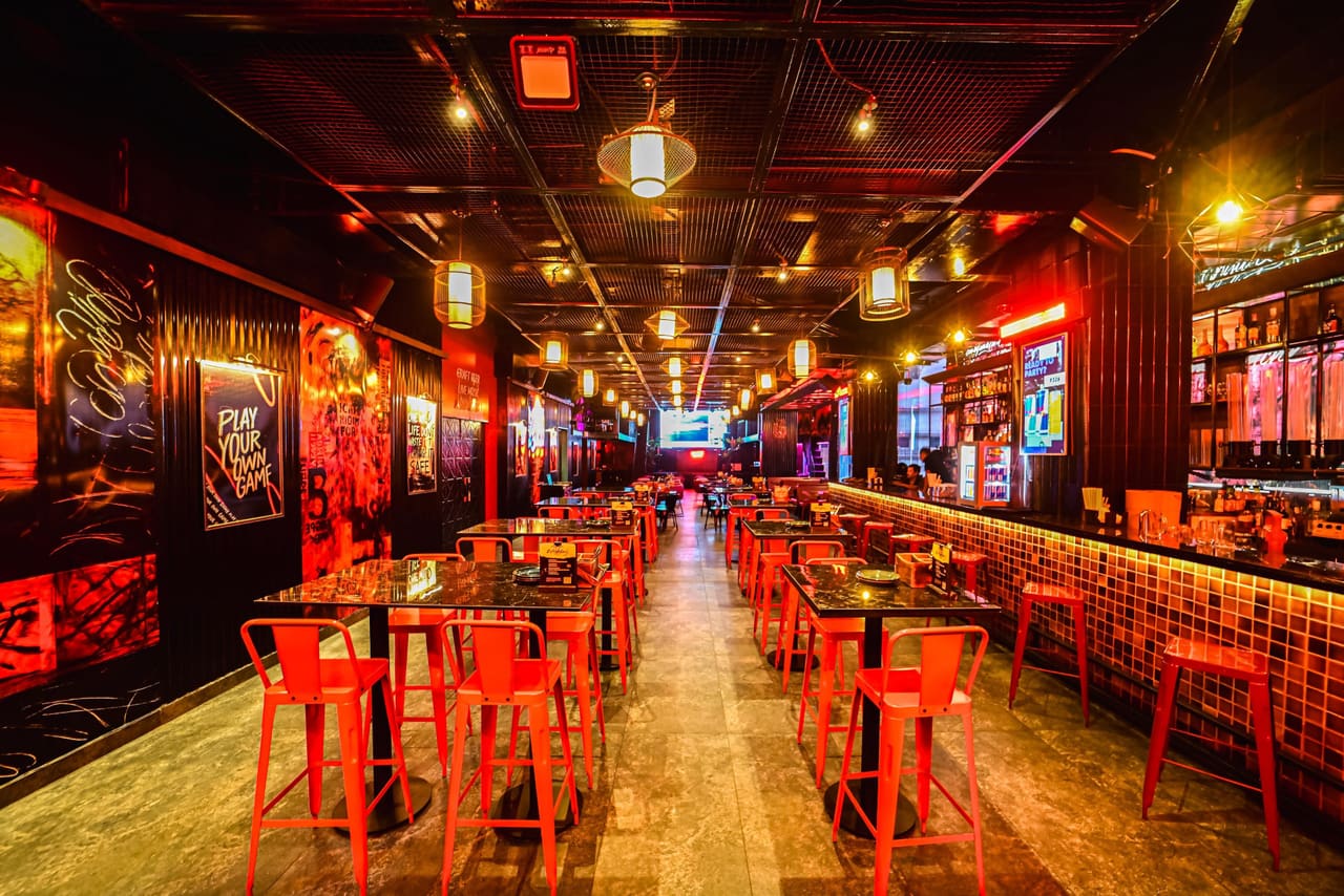 The Nuts & Brew main hall: red stools and high tables down a long room under pendant lights, a tiled bar along the right.
