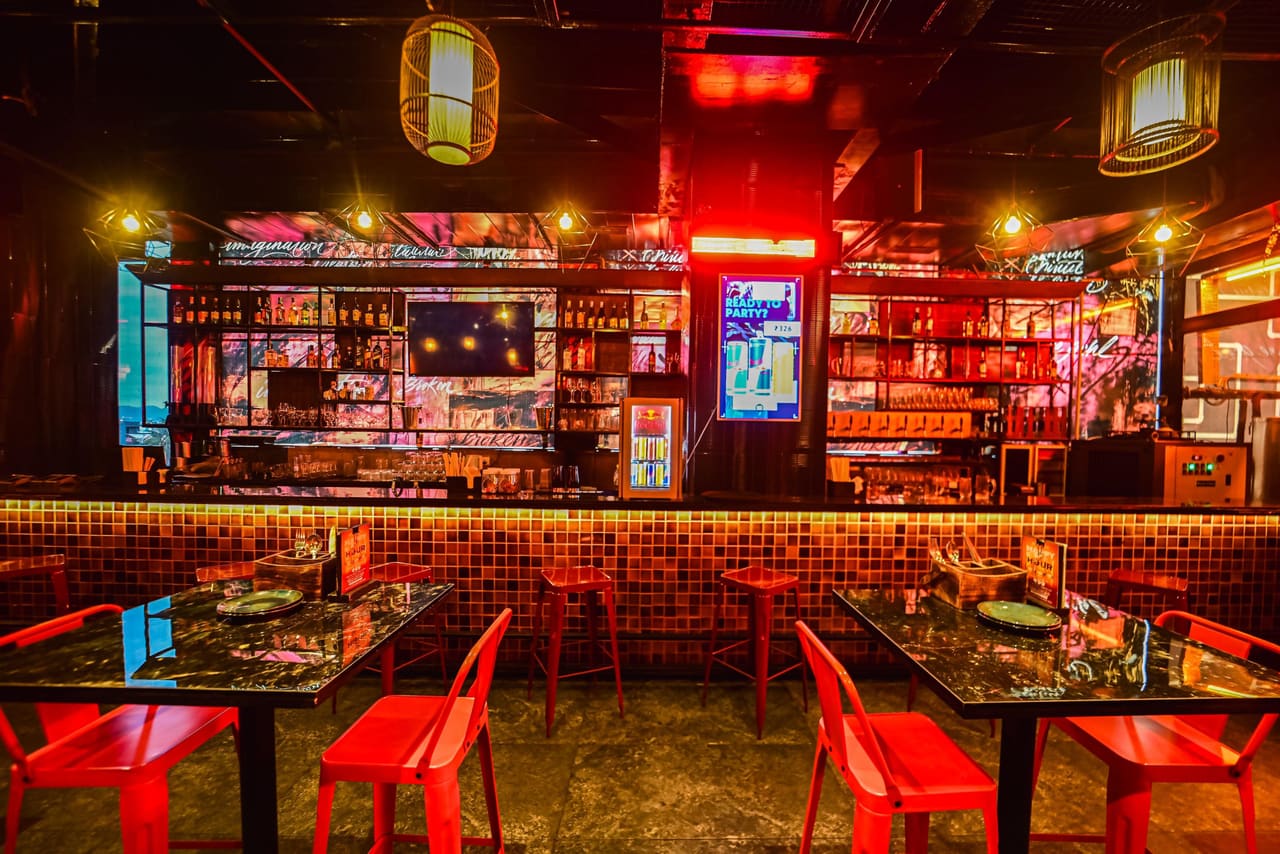 The Nuts & Brew bar seen head-on: a tiled counter and stools under red-lit shelving and screens.