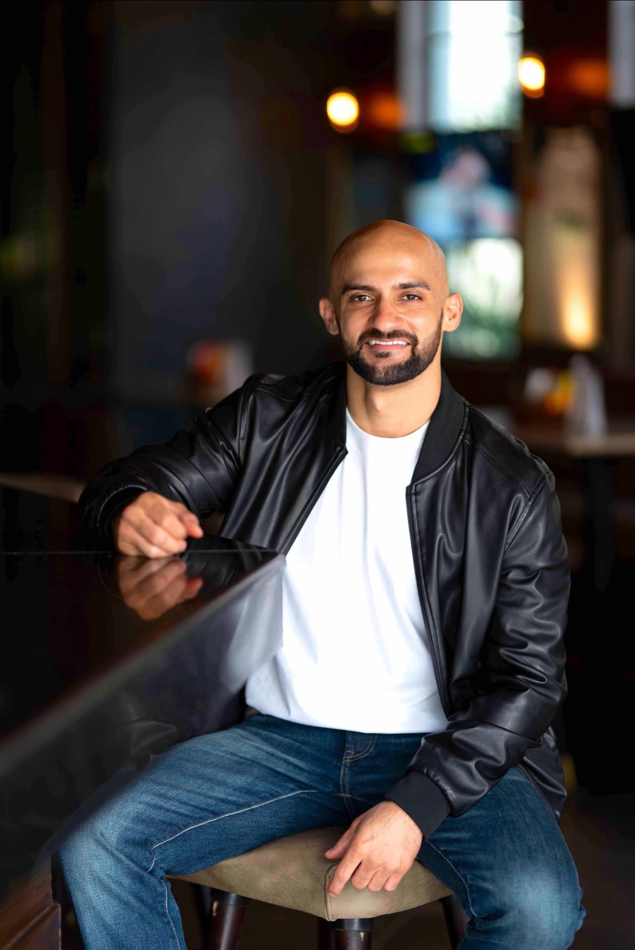 Rish Saini seated at a bar counter in a black leather jacket