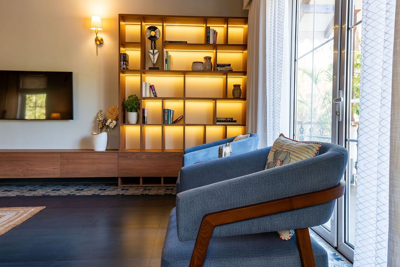 A reading corner with a blue armchair in front of backlit timber shelves