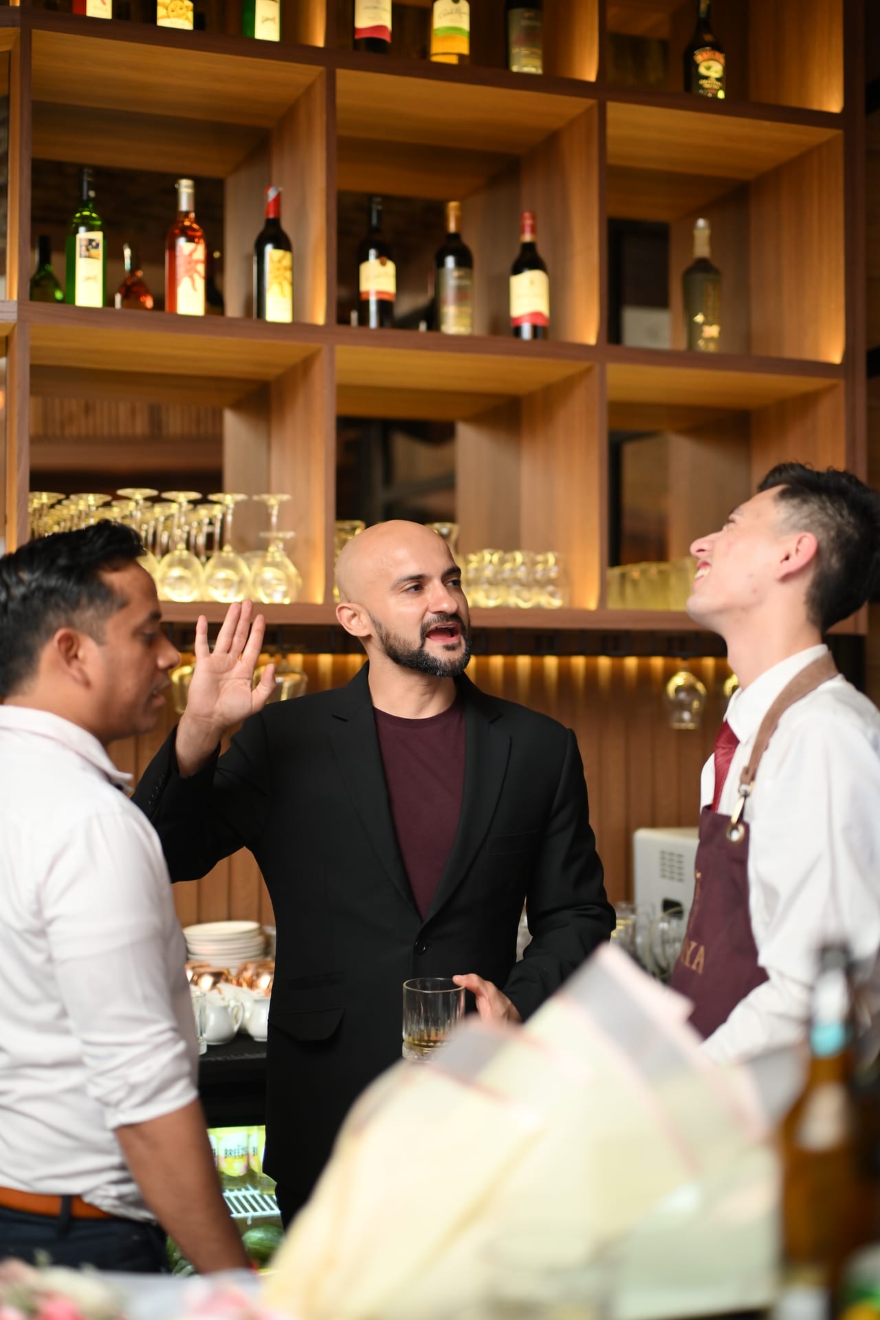 Rish Saini laughing with two bartenders behind the bar at Ālaya Café & Bar