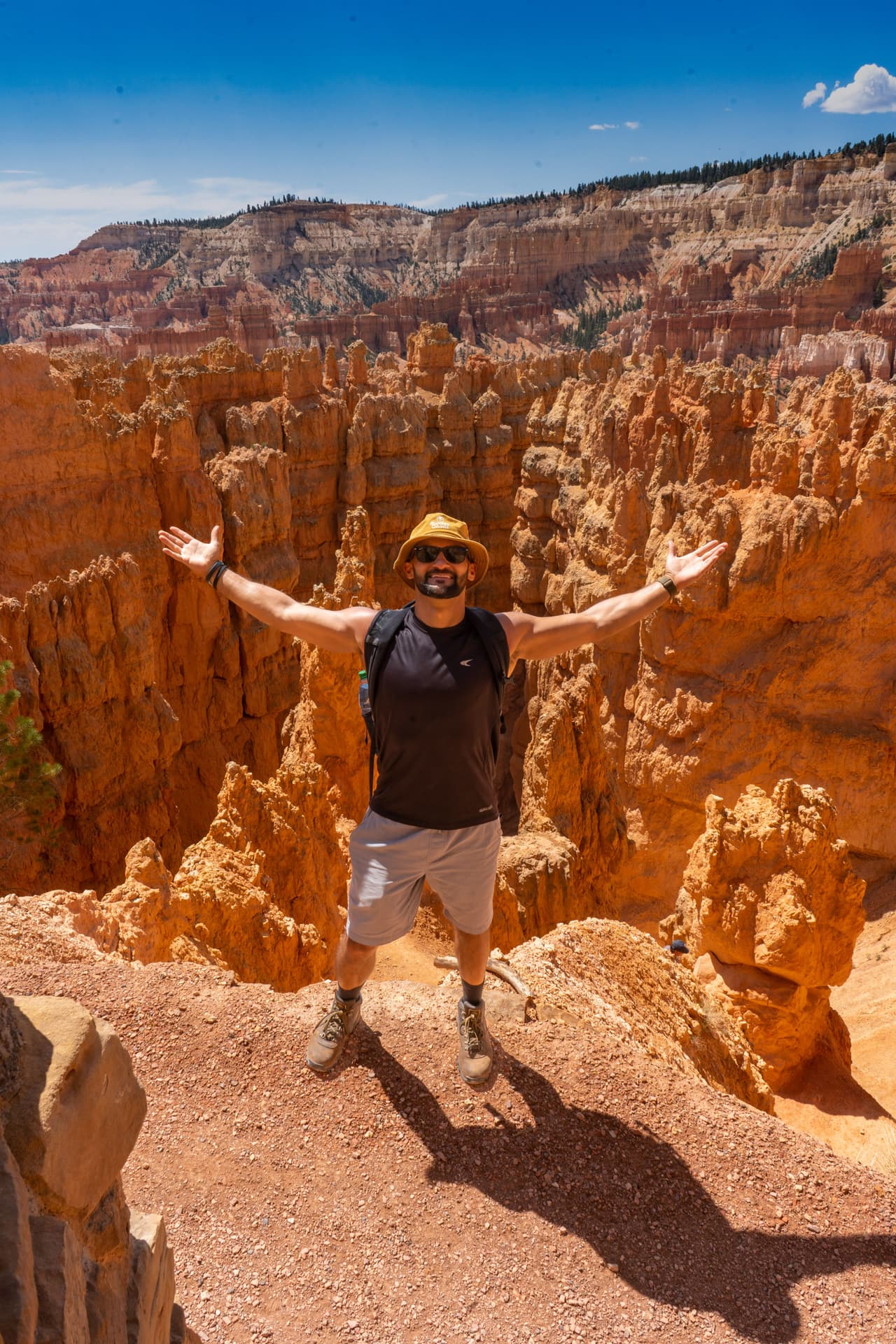 Rish Saini with his arms spread wide on a trail among the orange hoodoos of Bryce Canyon