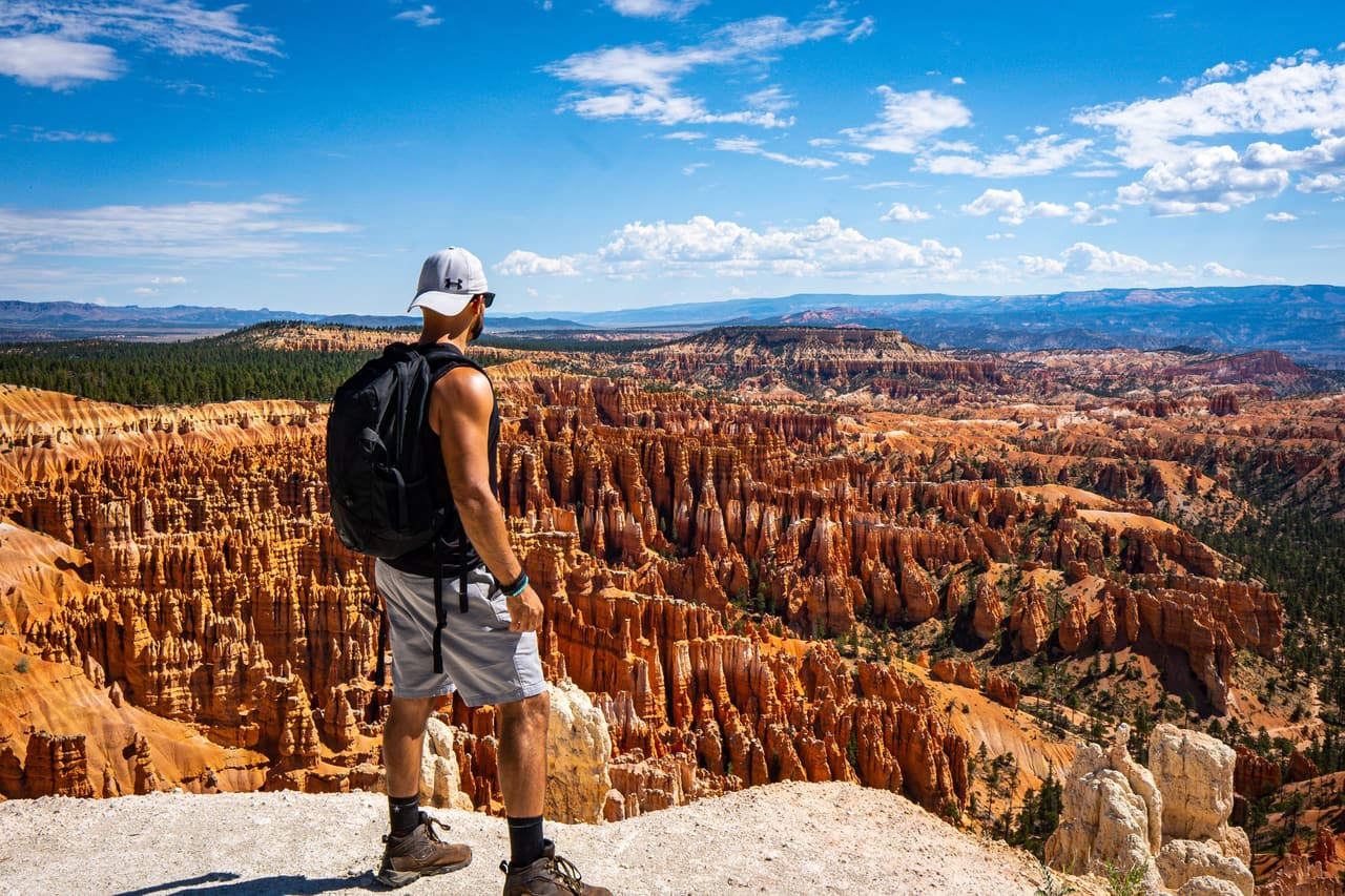 Rish Saini with a backpack and cap, standing on a rim above the hoodoo amphitheatre of Bryce Canyon