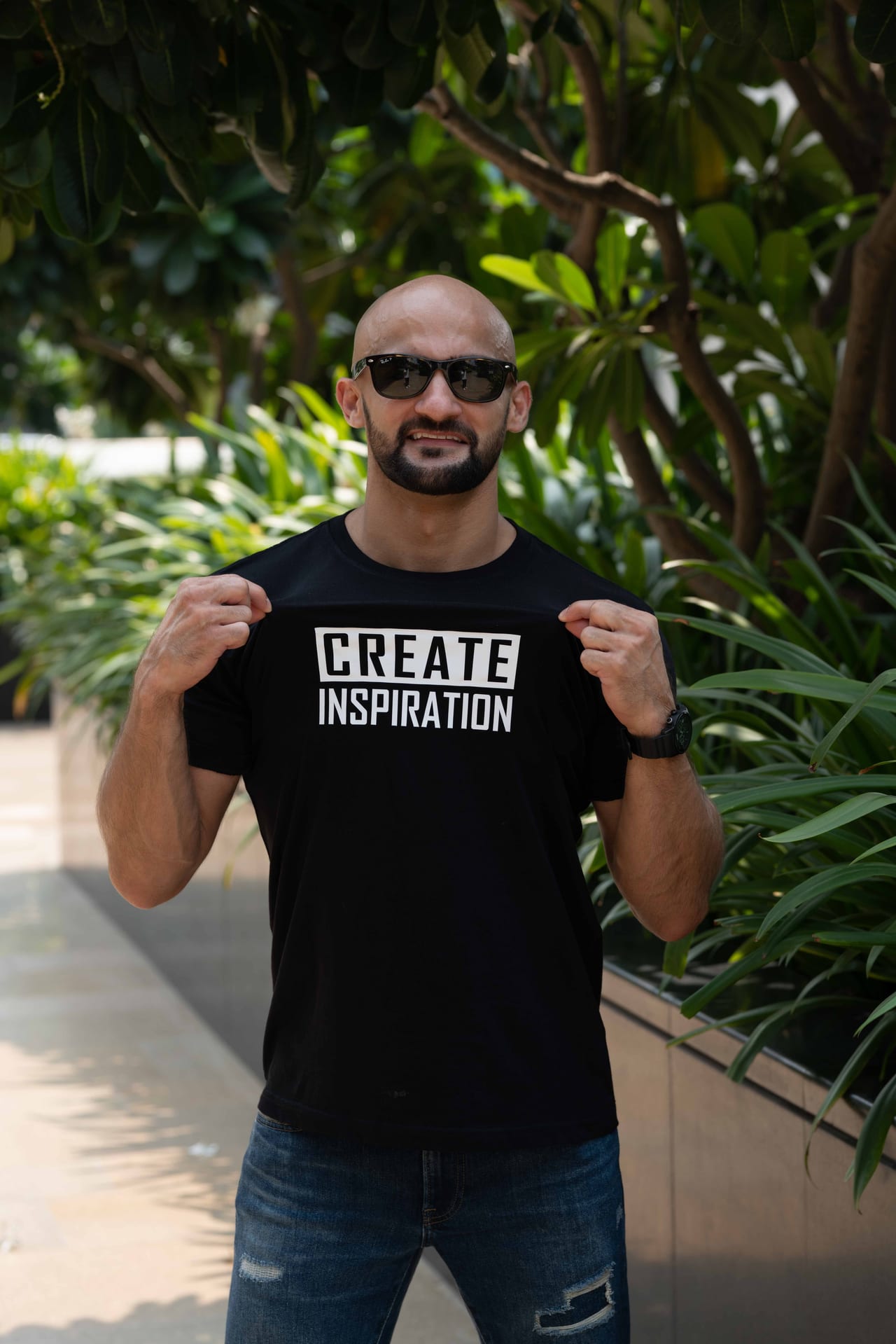 Rish Saini in sunglasses and a Create Inspiration T-shirt among tropical plants