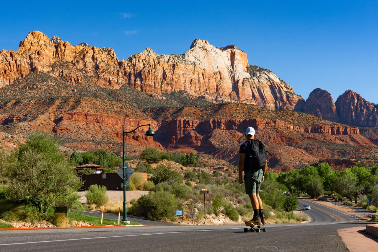 Rish Saini longboarding down a road with red sandstone cliffs and desert scrub behind him