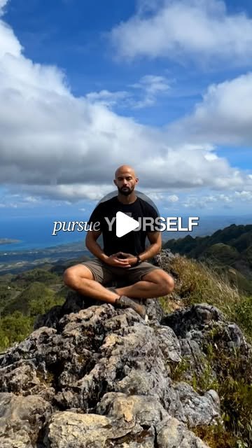 Rish Saini sitting cross-legged on a rock above green hills and the sea