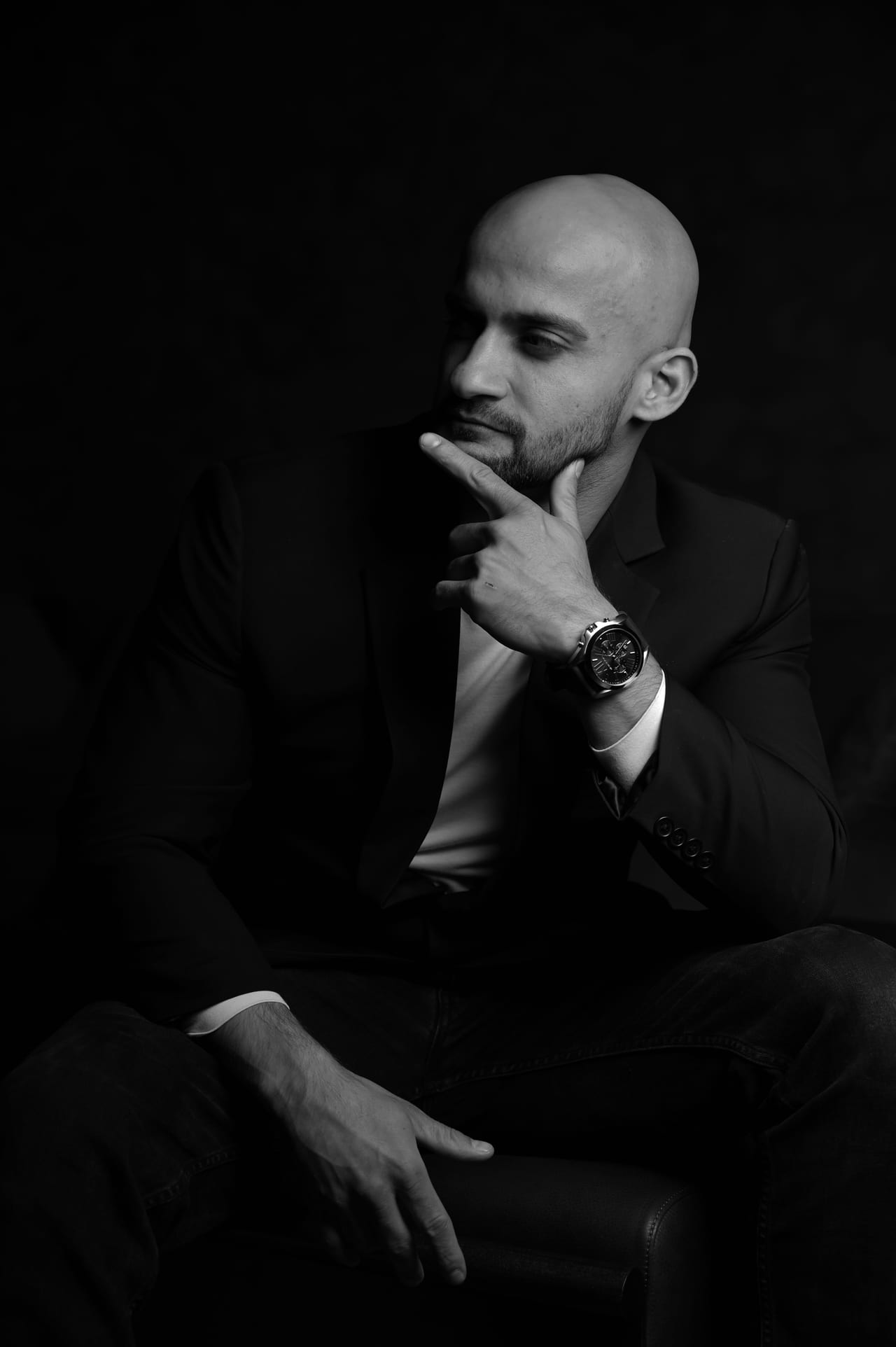 Black-and-white portrait of Rish Saini seated in a dark suit, his hand at his chin