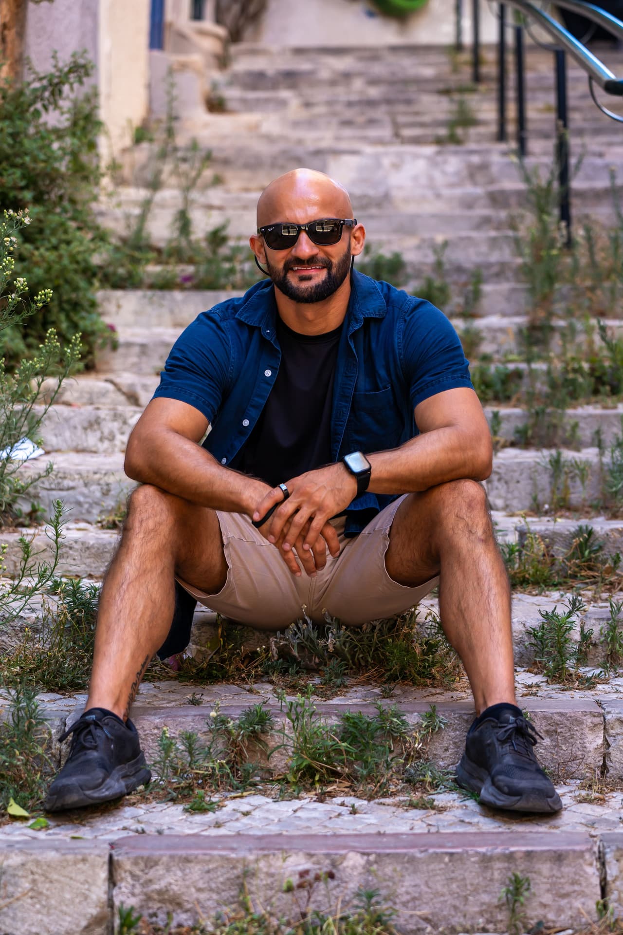 Rish Saini sitting on worn stone steps in sunglasses and a navy shirt, smiling