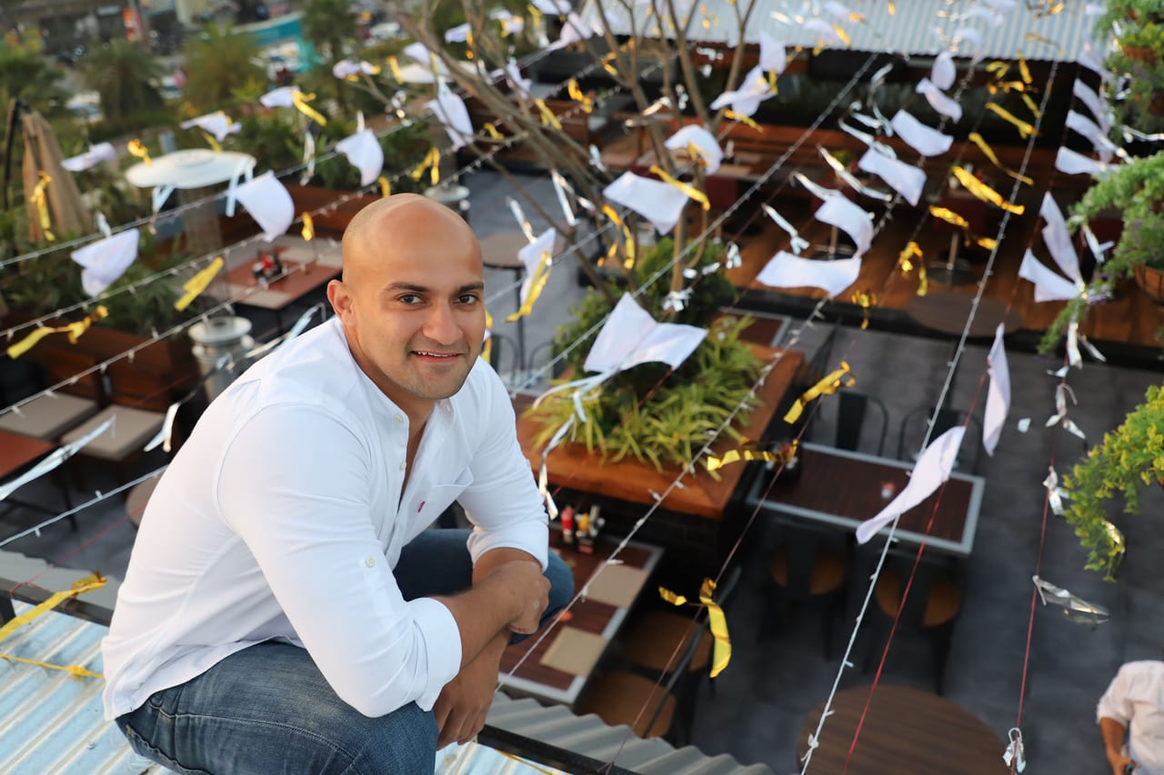 Rish Saini in a white shirt, crouching and smiling beside rows of planters on a terrace