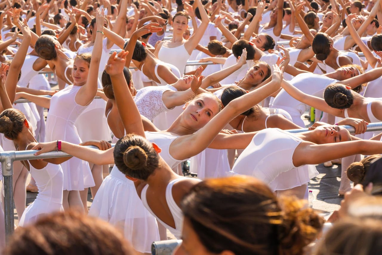A sea of dancers in white raising their arms in unison